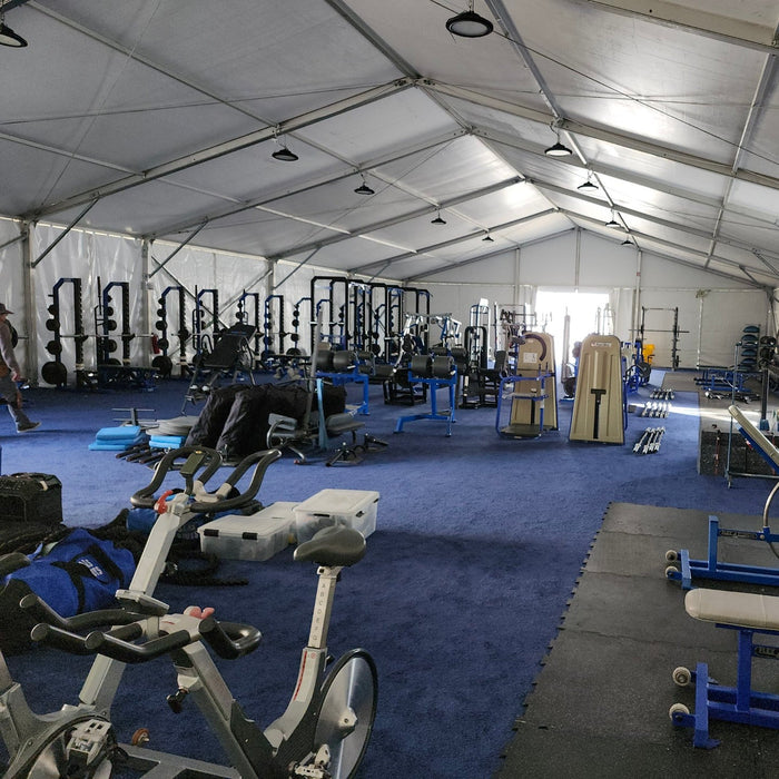 Spacious outdoor gym tent with blue carpet, weight equipment, and exercise bikes for effective workouts.
