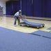 Man rolling out gray gym flooring on a cart in a gymnasium setting.