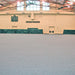 Large indoor sports facility with gray flooring and green protective barriers along the walls.