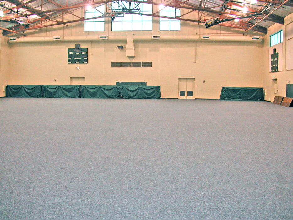 Large indoor sports facility with gray flooring and green protective barriers along the walls.