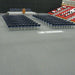 Arranged blue chairs on gray floor for an event, with a podium on a raised platform in a gymnasium.
